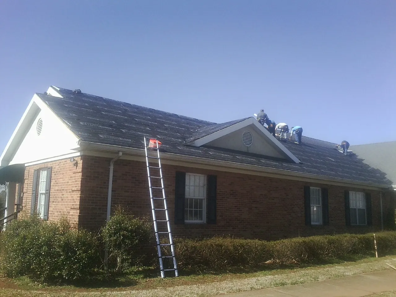 Crew tearing shingles off a brick ranch roof with a ladder set — Emergency Roof Repair work by our crew in David City