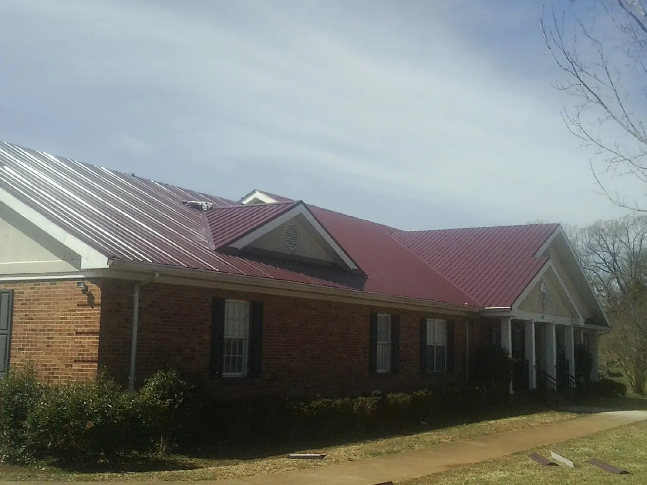 Red metal roof with gabled entries on a long brick building, from a Hail Damage Roof Repair job in David City