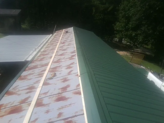 Old rusted panels beside newly installed green metal roofing — Wind Damage Roof Repair by Roofing Brothers in David City