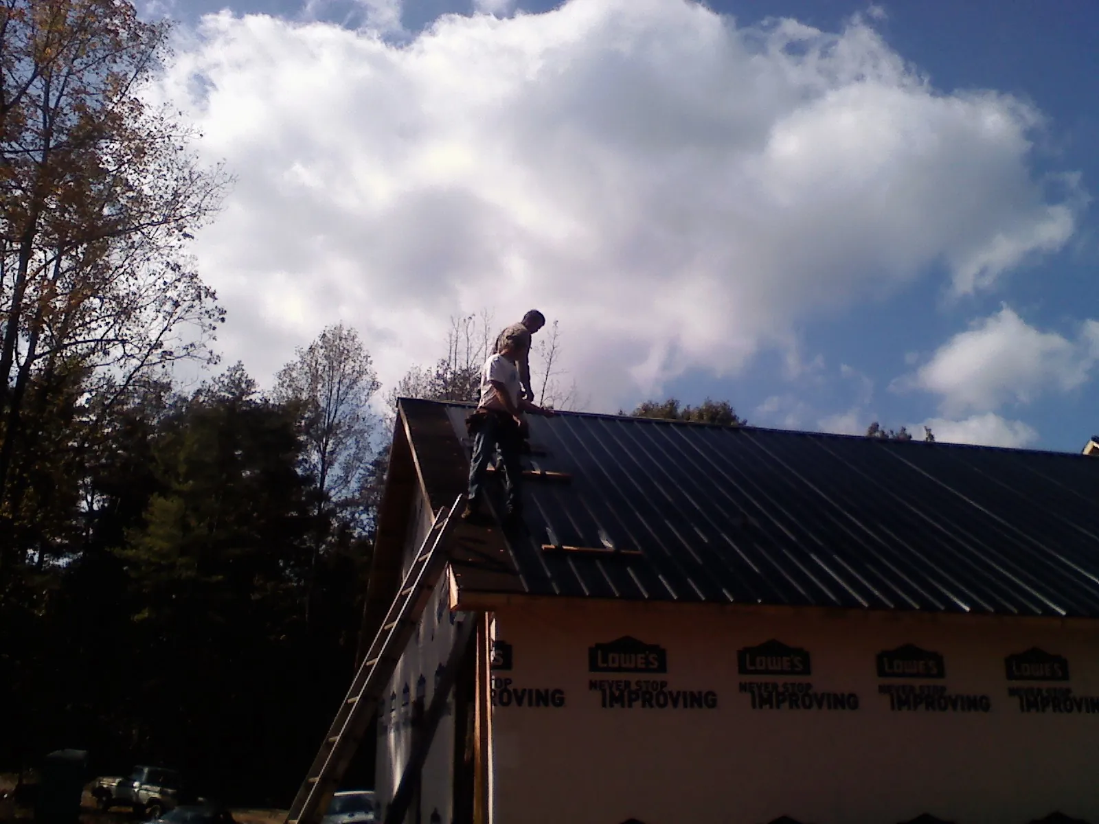 Roofer fastening dark metal panels high against a cloudy sky, from a Roof Inspection job in David City