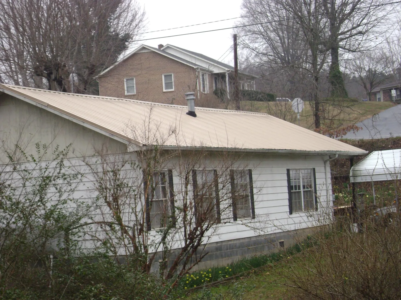 Tan metal roof on a white sided house set into a hillside — Commercial Roofing by Roofing Brothers in David City